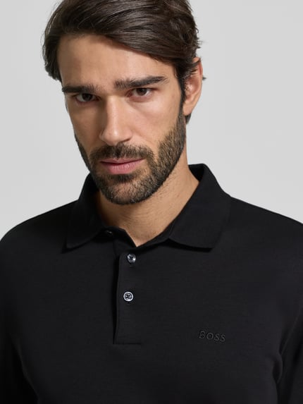 Męski model nosi Koszulkę polo z napisem z logo Poloshirt mit Label-Schriftzug od BOSS, bawełna, prosty krój, kołnierzyk polo, model 'Pado 30', listwa guzikowa, krój z długim rękawem, prążkowane zakończenia rękawów, długość tyłu 76 cm, rozmiar L, czarny kolor, gładka struktura, półzbliżenie na górną część ciała.
