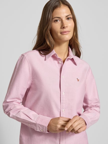 Kobiece modelka nosi bluzkę koszulową z bawełny o luźnym kroju z kołnierzykiem koszulowym, listwą guzikową i wyhaftowanym logo Polo Ralph Lauren; różowy kolor, długość tyłu 72 cm, długość rękawa 60 cm, widok na górną część ciała z przodu.