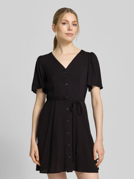 Vrouwenmodel draagt Leicht ausgestelltes Minikleid aus reiner Viskose Modell 'ALBA' van Vero Moda, look: effen, licht uitlopend, minilengte, V-hals, tailleriem, knoopsluiting, korte wijde mouwen, materiaal: zuiver viscose. Nahaufnahme bovenlichaam.