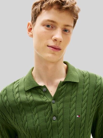 Männermodel trägt Regular Fit Strickpullover aus reiner Baumwolle von Tommy Hilfiger in grün mit Zopfmuster, Nahaufnahme Oberkörper.