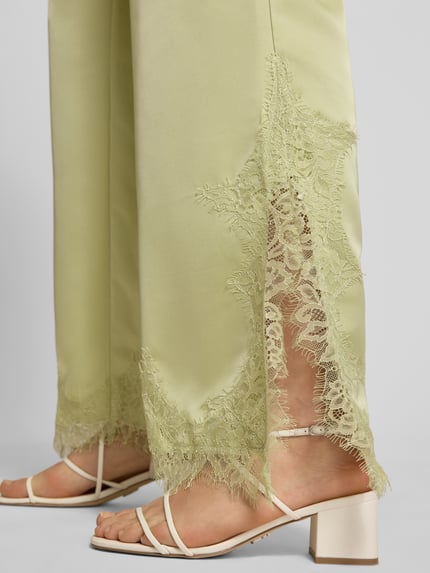 Frauenmodel trägt Flared Fit Stoffhose mit Spitzenbesatz von Gina Tricot in Satin-Optik, grün, Spitzenbesatz am Bein, Nahaufnahme Bein. Damen Stoffhose, elastischer Bund, Tunnelzug, Bundweite 40 cm, Innenbeinlänge 79 cm, Größe S.