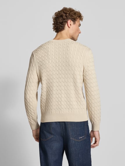 Männermodel trägt Regular Fit Strickpullover aus Baumwoll-Mix von Lacoste in Beige mit Zopfmuster, Herren Strickjacke, Ganzkörperansicht Rückansicht.