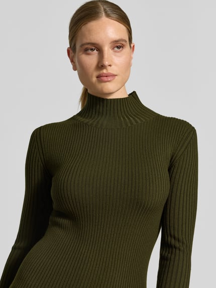 Frauenmodel trägt Longsleeve aus Woll-Mix von Victoria Beckham in Olivgrün, Ripp- und Strick-Optik, Stehkragen, Nahaufnahme Oberkörper.