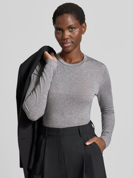 Frauenmodel trägt Longsleeve in melierter Optik von windsor, grauer Lyocell-Woll-Mix, gerader Schnitt, Rundhalsausschnitt, Label-Applikation, Ganzkörperansicht von vorne.