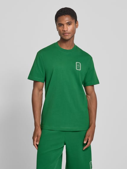 Männermodel trägt grünes Regular Fit T-Shirt aus reiner Baumwolle Modell 'CN Tenniscourt Backprint' von Lacoste, Herren T-Shirt, Ganzkörperansicht von vorne.