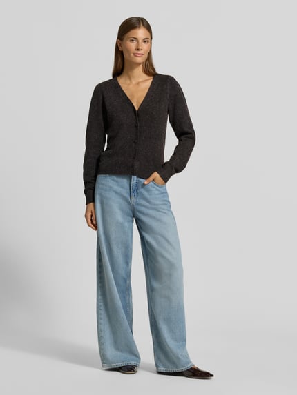 Frauenmodel trägt Regular Fit Strickjacke mit V-Ausschnitt Modell 'DOFFY' von VERO MODA in Dunkelgrau zu weiter Jeans, Ganzkörperansicht von vorne, Damen Strickjacke von VERO MODA.