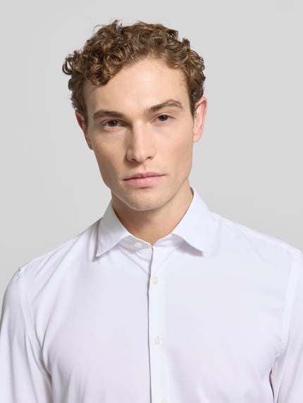Männermodel trägt Super Slim Fit Business-Hemd mit Knopfleiste von Jake*s, weiß, Kentkragen, Material-Mix mit Stretch-Anteil, Nahaufnahme Oberkörper.
