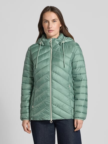 Frauenmodel trägt Regular Fit Steppjacke mit abnehmbarer Kapuze von s.Oliver RED LABEL in Uni-Optik, Reißverschlusstaschen, Ganzkörperansicht von vorne.