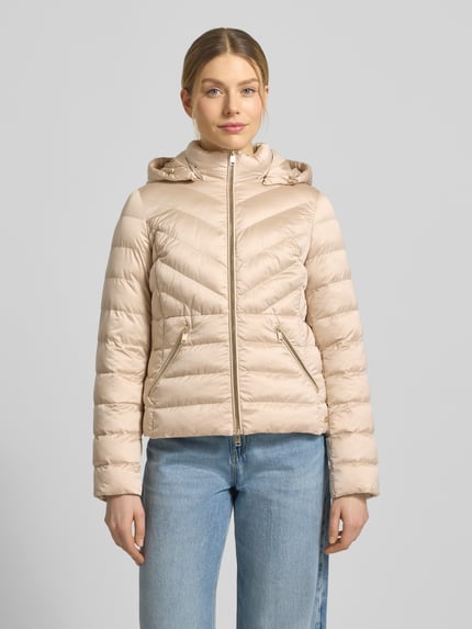 Frauenmodel trägt taillierte Steppjacke mit Zweiwege-Reißverschluss Modell 'ANYA' von Beaumont Amsterdam in Beige mit Kapuze, Ganzkörperansicht von vorne. Damen Steppjacke, Schnitt tailliert, Rückenlänge 55 cm, Schulterbreite 38 cm, Brustweite 48 cm, Ärmellänge 61 cm.