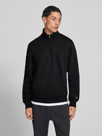 Männermodel trägt Sweatshirt mit Label-Details von Champion in Schwarz, Troyer-Kragen, Baumwollmischung, Ganzkörperansicht von vorne.