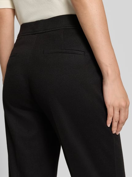 Frauenmodel trägt Boocut Fit Stoffhose mit Viskose-Anteil von Christian Berg Woman in Schwarz, sichtbare Paspeltaschen, Detailaufnahme Rückansicht.