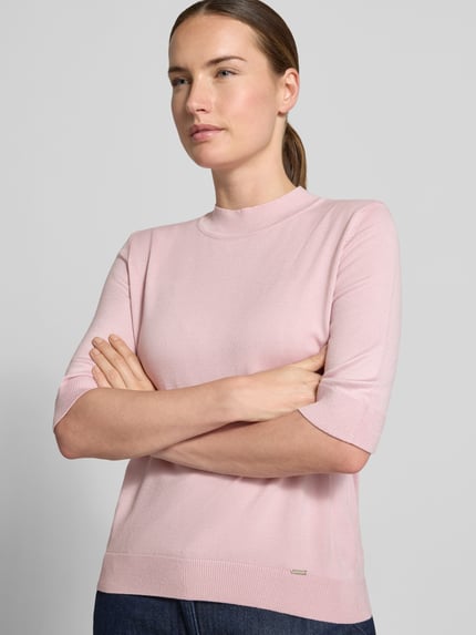 Frauenmodel trägt Strickpullover aus Viskose-Mix von MORE & MORE in Rosa, taillierte Passform und Stehkragen, Nahaufnahme Oberkörper.