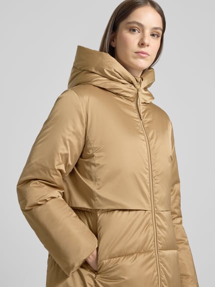 Frauenmodel trägt Steppmantel mit Kapuze Modell 'CARMEN' von JOOP! in Uni-Optik mit Teilungsnähten, Reißverschlüssen und Taschen, Nahaufnahme Oberkörper.