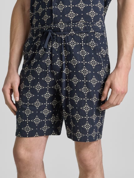 Męski model nosi Relaxed Fit Stoffshorts aus einer Baumwolle von s.Oliver RED LABEL, granatowy z beżowym wzorem, zbliżenie na dolną część ciała