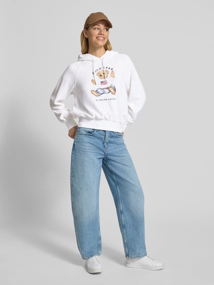 Kobiece modelka nosi Regular Fit Hoodie mit Polo-Bear-Print od Polo Ralph Lauren, bawełniany miks, kolor biały, krój regular fit, nadruk z przodu, frotte, pełny widok z przodu