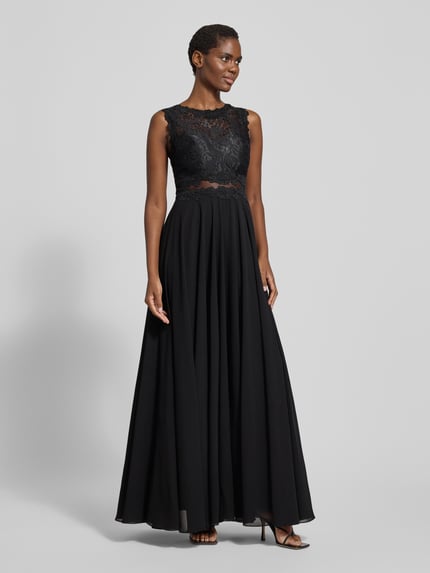 Frauenmodel trägt Abendkleid mit Spitze und Rundhalsausschnitt von Mascara, Maxikleid, schwarze A-Linie, Rückenlänge 153 cm, Brustweite 33 cm, Ganzkörperansicht von vorne.