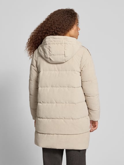 Frauenmodel trägt Steppmantel mit Kapuze Modell 'ONLDOLLY' von ONLY in einfarbigem Beige mit Struktur, Langform, Cord, Reißverschlusstaschen, Ganzkörperansicht Rückansicht.