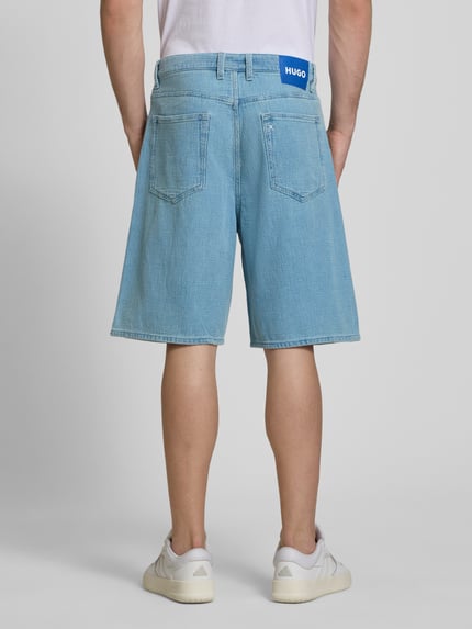 Männermodel trägt Loose Fit Jeansshorts aus reiner Baumwolle Modell 'MASON' von Hugo Blue in Denim-Optik mit Label Patch, Ganzkörperansicht Rückansicht.