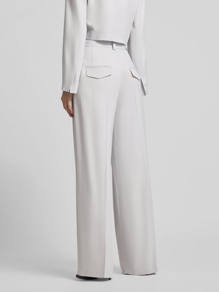 Frauenmodel trägt Weite Anzughose mit hoher Taille - curated by Vicky Heiler von SIC, helle Farbe, Wide Leg, Pattentaschen, Bügelfalten, Ganzkörperansicht Rückansicht.