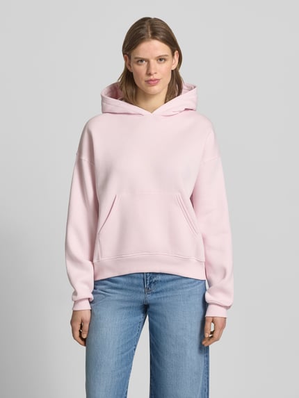Vrouwenmodel draagt Regular Fit Hoodie met kangoeroezak model 'Iconic' van Gina Tricot in lichtroze, katoenmix, regular fit, elastische boorden, dames, voorkant, volledige lichaamsweergave.