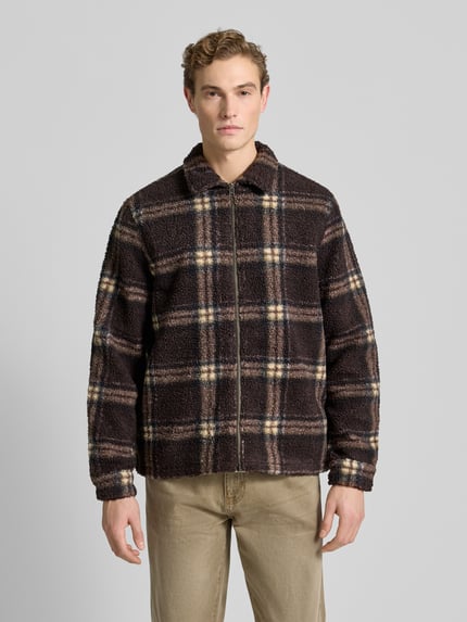 Männermodel trägt Hemdjacke mit Reißverschluss von Forét in braun-beigem Karomuster, Teddyfell, Reine Baumwolle, Ganzkörperansicht von vorne.