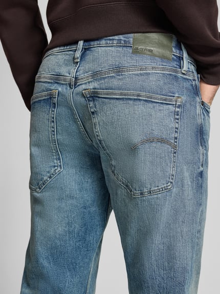 Mężczyznamodel nosi Slim Tapered Fit Jeans mit Eingrifftaschen Modell 'Streem' von G-Star Raw z czystej bawełny, niebieska tekstura z przetarciami, widoczne kieszenie, szerokość w rozmiarze 32/32: 44 cm, długość nogawki od wewnątrz: 80 cm, szczegółowe zdjęcie tyłu.