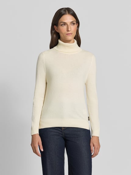 Frauenmodel trägt Regular Fit Rollkragenpullover aus Woll-Baumwoll-Mix von Barbour in Creme, glatte Struktur, dunkle Jeans, Ganzkörperansicht von vorne, Damen Rollkragenpullover von Barbour.