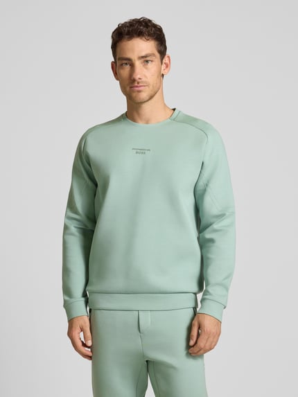 Męski model nosi Regular Fit Sweatshirt aus Baumwoll-Mix Modell 'SW_PS SPIRIT70 CN' od BOSS Green X Porsche, miętowy, długi rękaw, bawełniany miks, nadruk 3D, gładka faktura, okrągły dekolt, krój regular fit, całkowity widok z przodu.