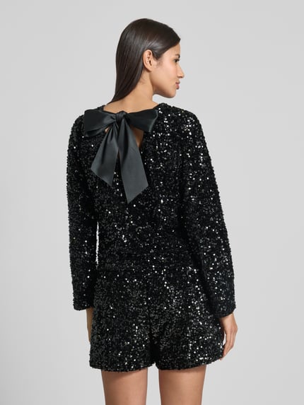 Frauenmodel trägt Regular Fit Langarmshirt mit Pailletten Modell 'CONFIDENCE' von Only, schimmernder Samt, Schleifen-Detail, tiefer V-Rückenausschnitt, Ganzkörperansicht Rückansicht.