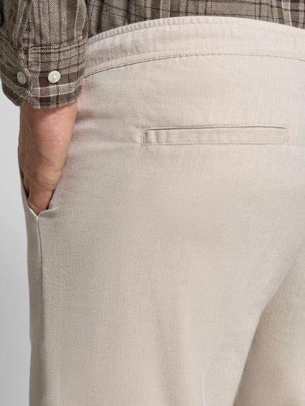 Mężczyzna nosi spodnie z elastycznym pasem model 'PILOU' od Casual Friday, mieszanka materiałów z lnem, krój regular fit, detal tylnej kieszeni, zbliżenie obszaru bioder