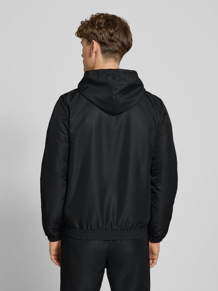 Männermodel trägt schwarzen Regular Fit Tracksuit mit Logo-Stitching Modell 'Carson' von SERGIO TACCHINI, elastische Abschlüsse, Kapuze, Reißverschluss, Eingrifftaschen, Rückansicht, Materialstruktur glatt.