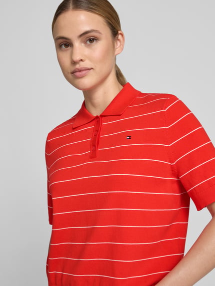 Frauenmodel trägt Regular Fit Pullover aus reiner Baumwolle mit Polokragen von Tommy Hilfiger für Damen in Rot mit weißen Streifen, Nahaufnahme Oberkörper.