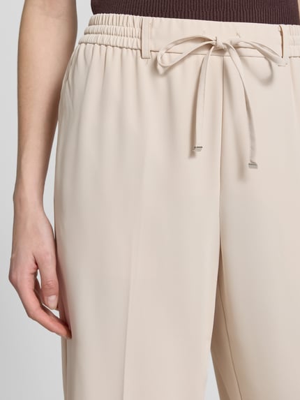 Frauenmodel trägt Wide-Leg-Pants mit elastischem Bund und Kordelzug, angedeutete Gesäßleistentasche, Modell 'Cevil ease' von Someday, Damen, beige, Schlupfhosen-Design, Nahaufnahme Oberkörper. Bundweite 36 cm, Innenbeinlänge 77 cm, Größe 36.