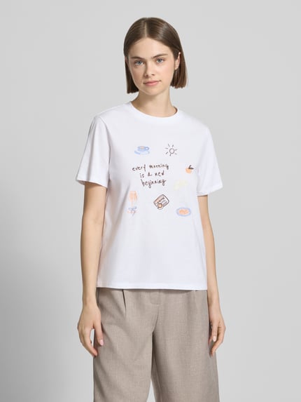 Frauenmodel trägt Damen T-Shirt von Pieces, Modell 'Regular Fit T-Shirt aus reiner Baumwolle Modell 'GAK', Optik: Unifarben, Passform: Regular-Fit, Applikation: Stickerei, Rundhals-Ausschnitt, Ärmelform: Kurzarm, Material: Reine Baumwolle, helles Weiß mit farbigen Stickereien, glatte Textur, Ganzkörperansicht von vorne.