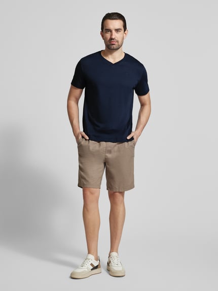 Mężczyznę model nosi Regular Fit T-Shirt aus reiner Baumwolle von Tom Tailor, kolor jednolity, krój regular fit, logo, dekolt V, krótki rękaw, jersey, bawełna. Ganzkörperansicht von vorne.