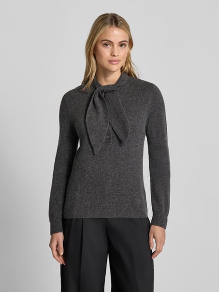 Frauenmodel trägt Strickpullover aus Woll-Mix mit Schluppe und Knopfleiste von Christian Berg Woman, dunkelgrau, Körperschmeichelnder Schnitt, Rundhalsausschnitt, Ganzkörperansicht von vorne. Rückenlänge 56 cm, Ärmellänge 65 cm.