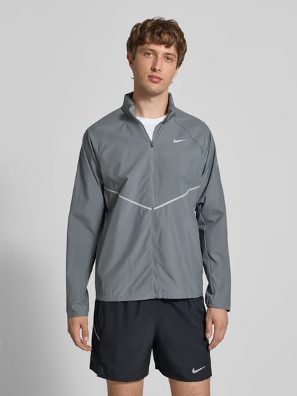 Männermodel trägt Regular Fit Jacke mit Stehkragen Modell 'Miler' von NIKE TRAINING in Grau mit Logo-Print und Reißverschluss, Ganzkörperansicht von vorne. Rückenlänge 67 cm, Ärmellänge 64 cm.