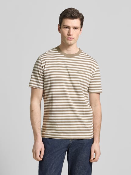 Männermodel trägt Regular Fit T-Shirt aus reiner Baumwolle von Marc O'Polo mit braun-beigen Streifen und Label Stitching, Ganzkörperansicht von vorne.