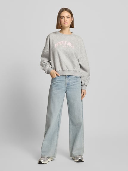 Frauenmodel trägt Sweatshirt mit Label-Print und Rundhalsausschnitt von Review aus Baumwoll-Mix im Relaxed-Fit, grau, Ganzkörperansicht von vorne.