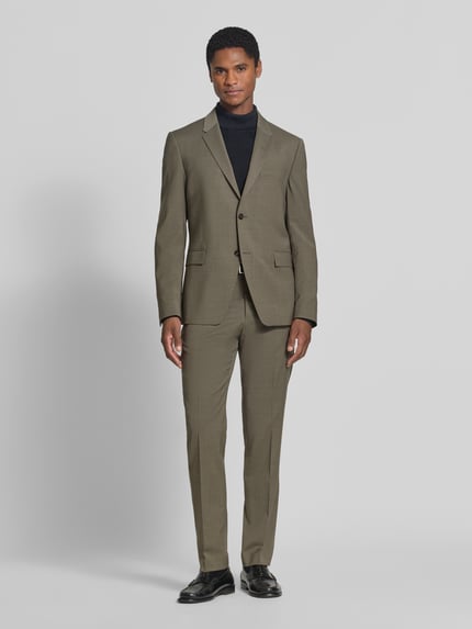 Männermodel trägt Regular Fit Sakko mit Woll-Anteil Modell 'Jamie' von Tiger of Sweden in Olive, feine Textur, glatte Oberfläche, Ganzkörperansicht von vorne. Sakko mit Reverskragen, 2-Knopfleiste, Pattentaschen, elastischer Material-Mix, Rückenlänge 73 cm, Schulterbreite 43 cm, Ärmellänge 66 cm.