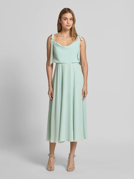 Frauenmodel trägt Knielanges Cocktailkleid mit Zierschleifen von Jake*s Cocktail in Mintgrün, Taillierte Passform, Ärmelloses-Design, blickdichter Unterrock, fließender Stoff, Ganzkörperansicht von vorne.
