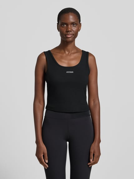 Vrouwenmodel draagt Slim Fit Top met Logo-Stitching model 'Circe' van Guess Activewear, elastische katoenmix, ronde hals, 29 cm ruglengte bij maat S, zwart, effen textuur. Volledig lichaamsaanzicht van voren.