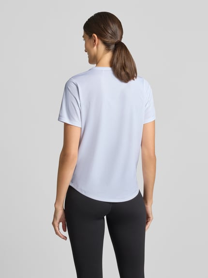Frauenmodel trägt T-Shirt mit Rundhalsausschnitt und Logo-Print von ASICS in Weiß, leicht abgerundeter Saum, Ganzkörperansicht Rückansicht.