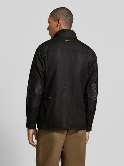 Männermodel trägt Funktionsjacke mit gewachstem Twill von Barbour in Schwarz, Stehkragen, Druckknöpfe, langarm, unifarben, Ganzkörperansicht Rückansicht.