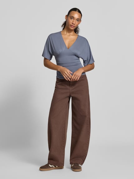 Frauenmodel trägt Bluse aus Viskose-Mix mit V-Ausschnitt von Gina Tricot, tailliert, halbarm, Farbe Blau, Ganzkörperansicht von vorne.