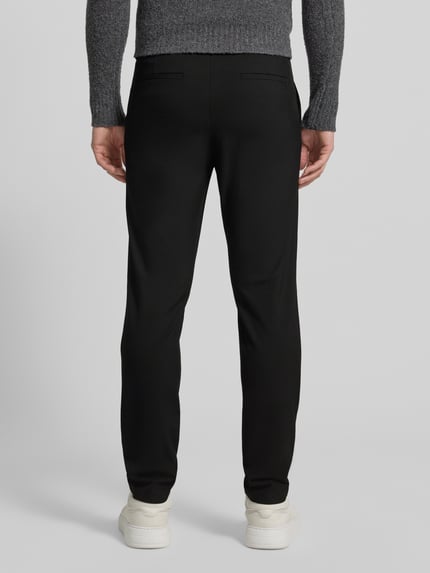 Männermodel trägt schwarze Chino mit Eingrifftaschen Modell 'ROBERT' von SELECTED HOMME aus Material-Mix mit Viskose-Anteil, Unifarbenes-Design, Körpernaher-Schnitt, Knopf- und Reißverschluss, Ganzkörperansicht Rückansicht.