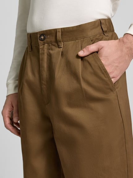 Männermodel trägt Bundfaltenhose mit Twillstruktur von Barbour in Braun, unifarben, sichtbare Bundfalte, Nahaufnahme Oberkörper.