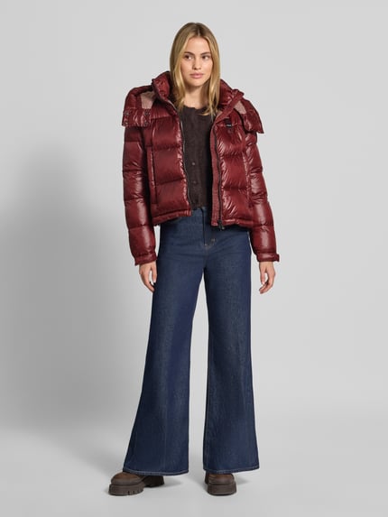 Frauenmodel trägt Regular Fit Jacke mit Sorona-Füllung Modell 'GLORIA' von Blauer USA in Stepp-Optik, bordeauxrot, glänzend, Ganzkörperansicht von vorne. Rückenlänge 52 cm, Stehkragen mit Kapuze, Zweiwege-Reißverschluss, Logo-Detail, Eingrifftaschen.