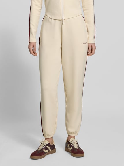 Frauenmodel trägt Jogpants mit Logo Modell 'JASMINE' von Guess Activewear aus cremefarbenem Material-Mix mit Lyocell, Nahaufnahme Oberkörper.