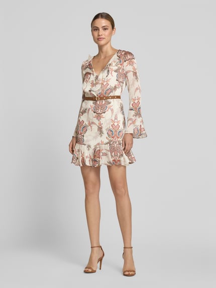 Frauenmodel trägt Minikleid mit Rüschenbesatz von GUESS, taillierte Passform, V-Ausschnitt, Langärmelig, Abnehmbarer Taillen, florales Muster, Rückenlänge 83 cm, Brustweite 42 cm, Ärmellänge 62 cm, Pastelltöne, lockere Textur, Ganzkörperansicht von vorne.